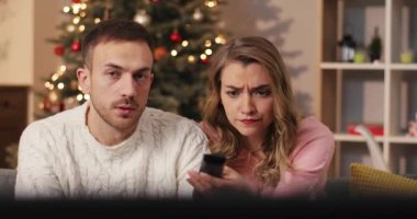 Kız ve erkek televizyon izleyip tartışıyorlar. Genç ve güzel bir kadın dekore edilmiş Noel ağacının arka planında televizyon kanallarını değiştiriyor. Kutlama atmosferi. Kapalı.