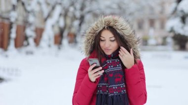 Kadın gülüyor ve telefonunda mesaj atıyor. Kız kış verandasında ve telefonu kullanıyor. Genç bir kadın, kış akşamı telefonuna mesaj atmaktansa kameraya gülüyor..