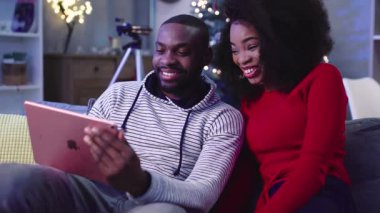 NEW YORK - 13 Aralık, 2017. İyi bir Afrikalı çift pazar akşamı tablette komedi seyrediyor. Gençler büyülenmiş Noel ağacının arka planında eğleniyorlar. Çıkma .