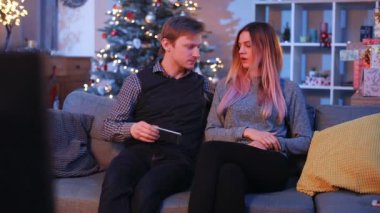 Kafkasyalı genç bir çift, güzel bir oturma odasında topları ve ışıklarıyla süslenmiş Noel ağacıyla kavga ediyor. Akıllı telefonu saklayan güzel kız. Gençler gülüyor. Kapalı.