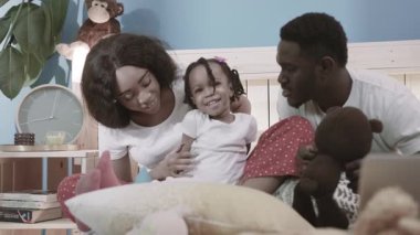 Afro-amerikan ebeveynlerin kızlarıyla evde yatakta oynamalarının sevimli görüntüsü. Evde çocuklu, gülümseyen bir çift.