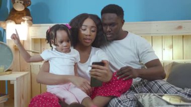Yatakta yatan güzel zenci anne ve babanın portresi. Gülümseyen mutlu aile evde akıllı telefondan selfie çekiyor..