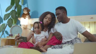 Güzel Afro-Amerikan ebeveynlerin portresi ve evde selfie çekerken kameraya gülümseyen sevimli kızları..