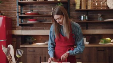 Sebze doğrayan güzel bir kızın portresi salata hazırlıyor. Güzel gülümseyen neşeli eş evdeki modern mutfakta öğle yemeği pişiriyor..