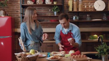 Gülümseyen genç bir çift mutfakta yemek pişiriyor, gülüyor, eğleniyor, sohbet ediyor, keyfine bakıyor, evde yemek hazırlıyor..