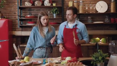 Komik evli çift birlikte yemek pişiriyor evdeki modern mutfakta müzik eşliğinde dans ediyorlar. İnanılmaz genç adam ve kadın hafta sonlarının tadını çıkarıyorlar..