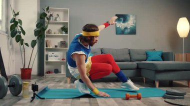 Egzersiz paspasının üzerinde dengede duran neşeli retro fitness adamı. Evde kamerada spor vlogcusu egzersizi yapıyor.