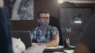 NEW YORK - 5 Nisan 2017: Sıradan giysiler içindeki çekici, ciddi bir adam masada oturuyor ve dikkatle dizüstü bilgisayarına bakıyor. Sakallı ve gözlüklü beyaz bir adam önemli müşterilerine mektup yazıyor..