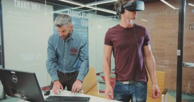 NEW YORK - 5 Nisan 2017: gündelik giysiler içinde şık, çekici bir adam etrafa bakıyor. Sanal gerçeklik gözlüklü sevimli genç adam yeni icadı test ediyor, bilgisayar kullanıyor..