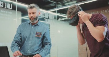 NEW YORK - 5 Nisan 2017: Sakallı yetişkin bir adam ve dijital gözlükleri test eden genç çekici bir adam. Başka bir gerçekliğe bakan mutlu beyaz adam. Gülümsüyor.