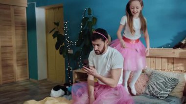 Peri elbiseli, yatakta akıllı telefon kullanan yorgun bir gencin portresi. Mutlu prenses dans edip sihirli değneğini sallayarak evde babasıyla oynuyor..