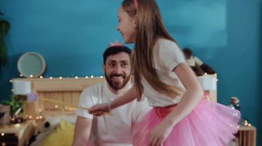 Sosyal genç baba, kızıyla eğleniyormuş gibi davranarak akıllı telefon kullanmakla meşgul. Peri gibi giyinmiş tatlı küçük kız yatakta dolaşıp babasını neşelendirmeye çalışıyor..