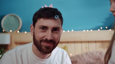 Yakın plan mutlu adam doğum günü partisi için kızıyla oynuyor. Yakın plan, neşeli küçük kız babasının kafasına saç tokası takıyor ve yatak odasında gülümsüyor..