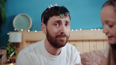 Kızıyla oynarken kameraya çekilen saç tokalarıyla yakın çekim zavallı genç baba. Genç heyecanlı kız babasını giydiriyor. Kutlama partisindeki prenses gibi gülümsüyor..