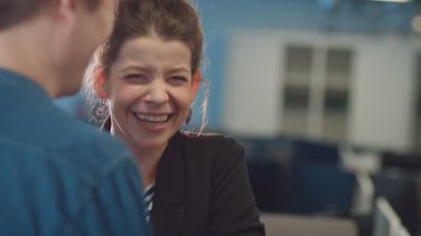 Saçları düzgün ve günlük kıyafetleri olan güzel bir kız. Erkeklerin şakalarına yüksek sesle gülüyor. Kız elleriyle ağzını kapatıyor. İletişim kuran genç meslektaşlarım.