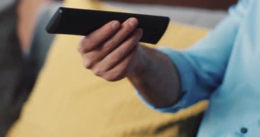 Evdeki rahat bir kanepede dinlenirken uzaktan kumandayı rahatça tutan elleri gösteren detaylı bir manzara.