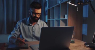 Tutkulu ve kendini işine adamış bir birey gece geç saatlerde şık, iyi ışıklandırılmış bir ev ofisinde çalışır.