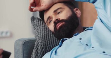 Rahat sakallı bir adam yumuşak bir kanepeye uzanıyor, dikkatle televizyon izliyor, sıradan bir yaşam tarzını yansıtıyor.