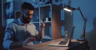Bir adam loş bir odada dizüstü bilgisayarına dikkatle odaklanır ve üretkenlik için konsantre bir atmosfer yaratır.