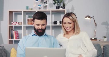 Bir çift, modern dekor elementleriyle çevrili sıcak ve rahat bir ev ortamında dizüstü bilgisayarda birlikte çalışıyor.