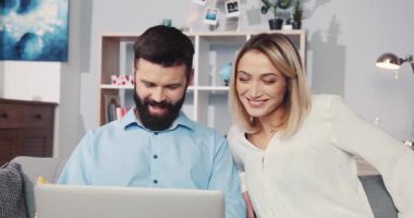 Bir çift rahat bir oturma odasında dizüstü bilgisayar üzerinde çalışırken mutlu bir şekilde birlikte vakit geçiriyorlar.