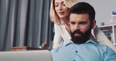 Sakallı bir adam, bilgisayarını modern ve şık bir ofis ortamında kullanırken yoğun bir şekilde işiyle meşgul olur.