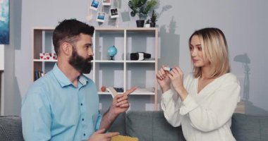 Sıcak ve modern bir oturma odasında, sakallı bir adam ve sarışın bir kadın birlikte canlı bir tartışmaya giriyorlar.