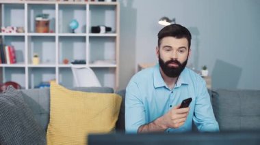 Bir adam yoğun bir rahatlık ve rahatlıkla çevrili modern bir oturma odasında televizyon izlemekle meşgul.