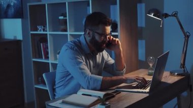 Kendini işine adamış bir adam bilgisayarını loş bir odada parlayan bir ekrandan yararlanıyor.