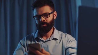 Akıllı telefonuyla yoğun bir şekilde meşgul olan bir adam, akşamları loş bir alanda, düşüncelere dalmış.