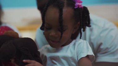 Afro-Amerikalı neşeli genç bir ailenin portresi evde, yatakta yatıyordu. Saçları örgülü şirin küçük bir kızın ailesiyle otururken oyuncağıyla oynadığı yakın plan..