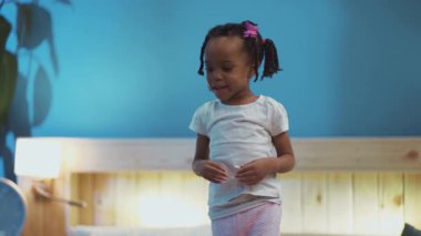 Harika bir Afrikalı Amerikalı çocuk evde eğleniyor. Saçlarına dokunan, yatakta duran şirin küçük kız portresi..