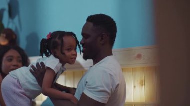 Mutlu bir Afrikalı babanın güzel portresi. Kızını kucağında tutuyor. Mutlu, genç bir aile ve çocuk yatakta dinleniyor..