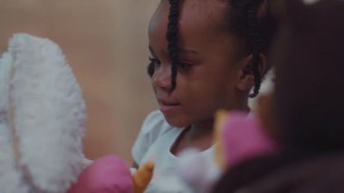 Çok hoş bir Afrikalı küçük kızın yakın plan portresi. Saçları örgülü ve evde en sevdiği oyuncaklarıyla oynuyor..