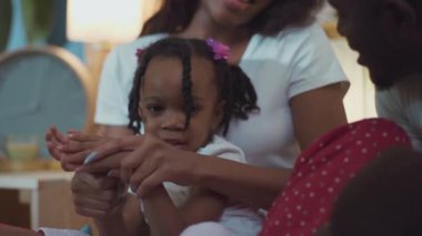 Annesinin kucağında oturan, yatakta el çırpıp oynayan Etiyopyalı küçük kızın yakın çekimi..