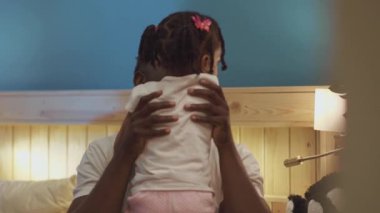 Küçük tatlı gülümseyen Afrikalı Amerikalı kız. Evdeki odada babasına sarılıyor..