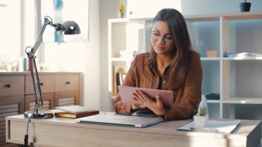 Kahverengi gömlekli güzel kız elinde pembe tablet ve dokunmatik ekranlı dairede modern onarım ile. Genç kadın oyun oynuyor, kazanıyor..