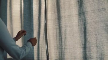 Beyaz bluzlu, kahverengi saçlı genç bir kadın sabah pencereye gelip perdeleri açıyor. Gülümseyen kız pencereden şehre bakıyor..