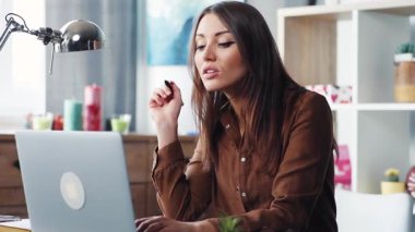 Laptop 'ta çalışan kahverengi gömlekli güzel, genç, kahverengi saçlı bir kadın. Sevimli bir kız klavyeye bilgi giriyor, not defterine bir şeyler yazıyor. Gülümsüyor.