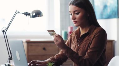 Kredi kartına bakan güzel, kahverengi saçlı bir kadın. Güzel bir kız internet bankacılığı kodunu giriyor. Kapalı.