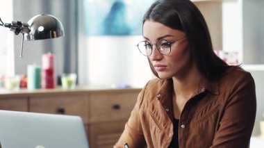 Dizüstü bilgisayarın başında oturan çekici ve zeki bir kadın. Not defterine not alıyor. Gözlüklü, işini bitiren, dizüstü bilgisayarının kapağını kapatan hoş bir kız..