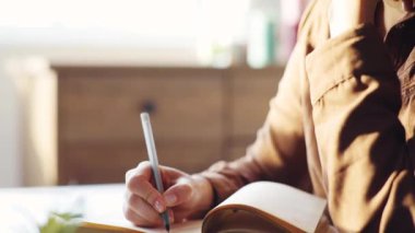 Gözlüklü güzel beyaz kız masada oturuyor ve günlüğünü yazıyor. Kafa kafaya tutuşan düşünceli bir kız. Yakın plan. Profil.