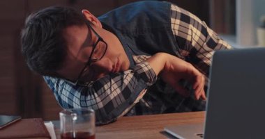 Tamamen bitkin bir genç adam laptopuyla geç saatlere kadar çalışırken dağınık masasında uyuyakaldı.