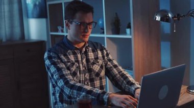 Bir adam gece geç saatlere kadar çalışıyor. Yanında bir fincan çay içerken kendini dizüstü bilgisayarına kaptırmış.