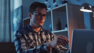 Genç bir adam gece geç saatlerde işine odaklanmış ve kararlı bir şekilde dizüstü bilgisayarıyla meşgul olur.