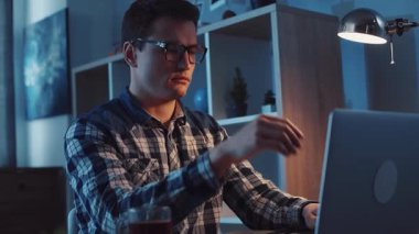 Genç bir adam rahat, ortam aydınlatmalı bir odada otururken kendini dizüstü bilgisayarına kaptırdı.