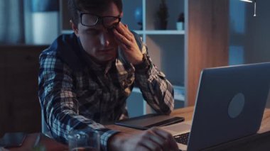 Yorgun bir birey gece bir dizüstü bilgisayarın üzerine yığıldı, modern iş kültüründe stres ve yorgunluğu simgeliyor..