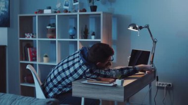 Uzun çalışma saatlerinden yorgun düşmüş yorgun bir öğrenci kafasını kitaplarla dolu bir masanın üzerine koyar.