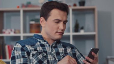Genç bir adam şık ve çağdaş bir oturma odasında rahatça otururken akıllı telefonuna odaklanır.