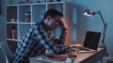 Genç bir adam gece geç saatlere kadar bilgisayarının başında çalışırken kendini bunalmış ve stresli hisseder.